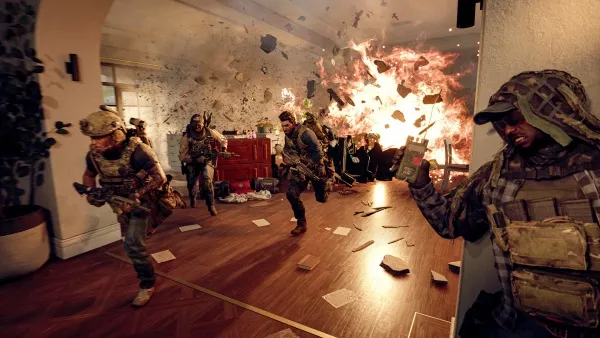 A group of soldiers in combat gear are advancing through a room with debris scattered on the floor. Explosions and fire erupt from an adjacent room, creating a chaotic scene. The soldiers appear focused and ready for action, with weapons drawn and tactical equipment visible. The setting suggests a high-stakes military operation or mission.