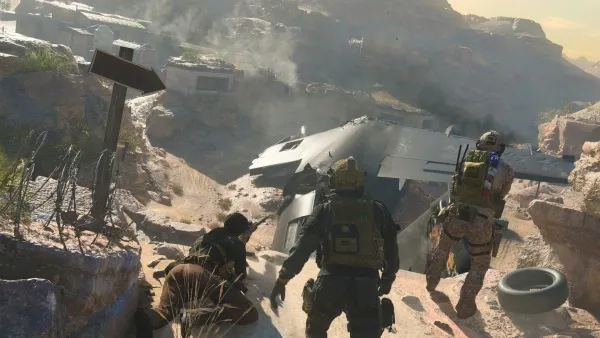 A group of soldiers in combat gear are navigating a rocky, mountainous terrain. They appear to be on a mission, with one soldier carrying a large backpack and another holding a rifle. In the background, there is a crashed aircraft and smoke rising from a distant village or settlement. The scene suggests a post-apocalyptic or war-torn environment.