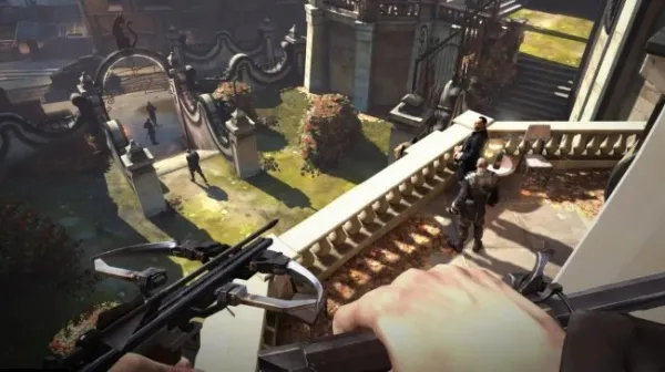 A first-person perspective of a person holding a crossbow, overlooking a courtyard with statues and an archway. The scene is set in a historical or fantasy setting with stone architecture and greenery. The lighting suggests it's daytime with sunlight casting shadows on the ground.