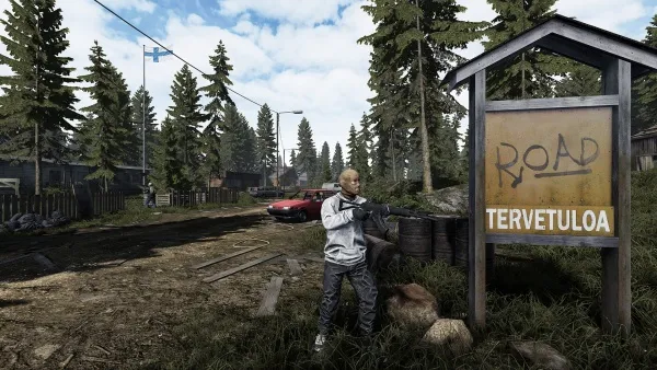 A man in a white jacket and blue jeans stands on a dirt road, holding a gun. He is positioned next to a wooden sign that reads "ROAD" and "TERVETULOA." The background features tall pine trees, a red car parked by the roadside, and some buildings partially obscured by foliage. The sky is partly cloudy, suggesting an overcast day. The scene appears to be set in a rural or semi-rural area.