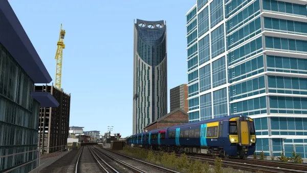 A modern cityscape with a sleek, blue and yellow train traveling on elevated tracks. The scene includes contemporary glass buildings, one of which is under construction with a towering crane nearby. The sky is clear and blue, suggesting a bright day in an urban environment.